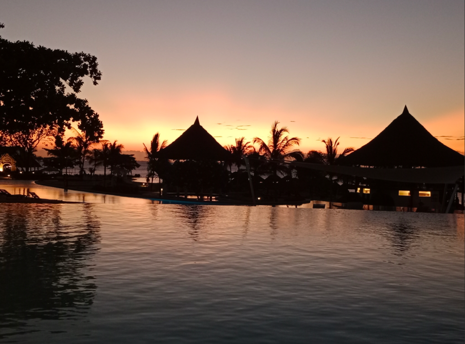 Sagome di strutture in paglia e palme riflesse nell'acqua di una piscina a sfioro al tramonto sulla spiaggia di Nungwi.