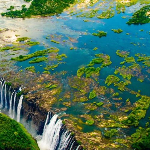 Fotografia aerea che mostra le imponenti cascate d'acqua che precipitano nella gola profonda tra fitta vegetazione e isole fluviali in Zambia.