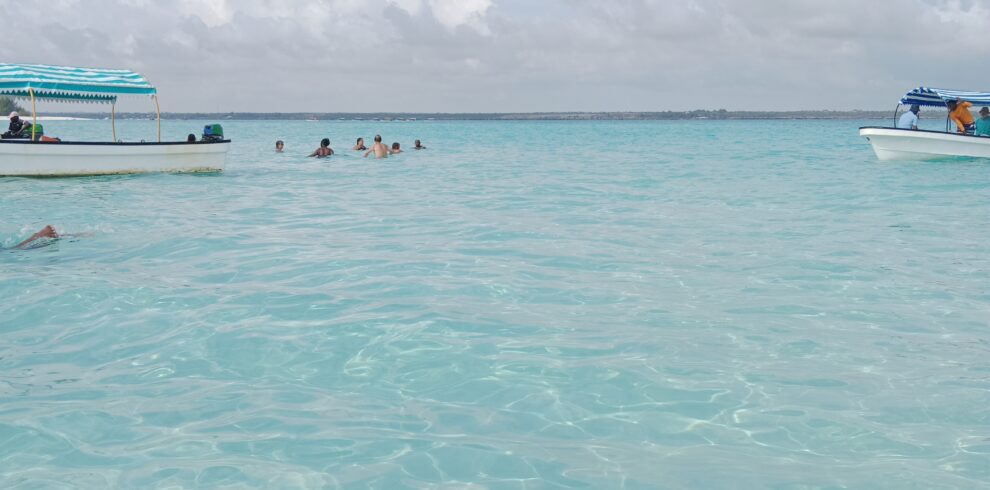 Persone che nuotano nelle acque limpide e turchesi dell'Oceano Indiano a Zanzibar con piccole imbarcazioni ai lati.