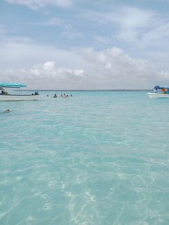 Persone che nuotano nelle acque limpide e turchesi dell'Oceano Indiano a Zanzibar con piccole imbarcazioni ai lati.