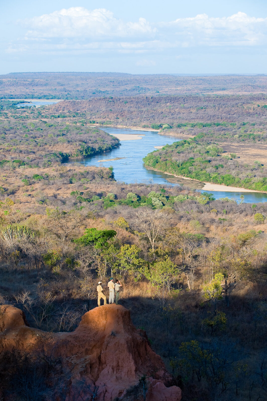 Tre persone osservano dall'alto di una roccia un'ansa del fiume Okavango che attraversa la vegetazione.